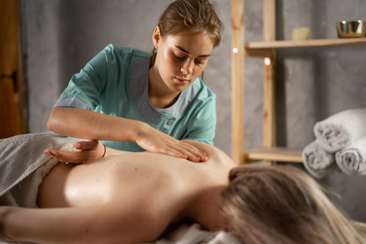 masseur massaging shoulder of young woman. Female patient getting remedial body and shoulder blade massage easing pain and relaxing muscles. Professional masseur or manual therapist massaging